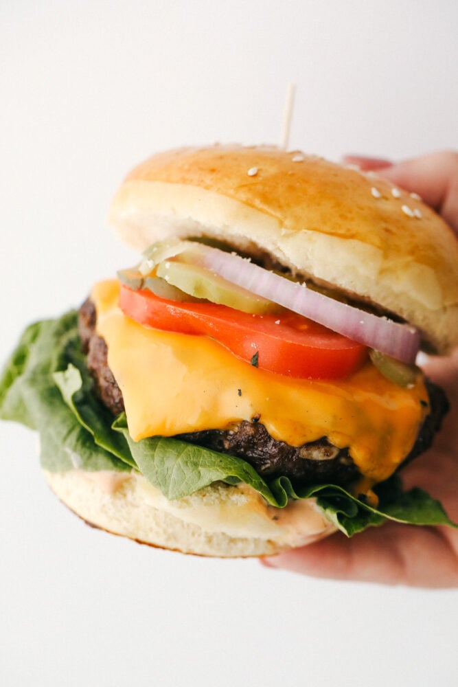 Grilled Beef Burgers are one of the most amazing things you can sink your teeth into, especially when they are done right! Be prepared, because these will be the best burgers you have ever had! Holding a perfect juicy hamburger with toppings on a homemade bun.