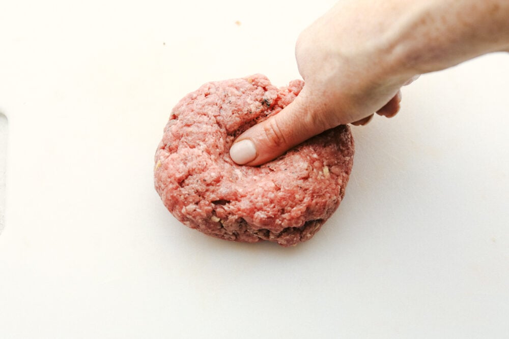 Grilled Beef Burgers are one of the most amazing things you can sink your teeth into, especially when they are done right! Be prepared, because these will be the best burgers you have ever had! Putting a divot in the burger with a thumb.