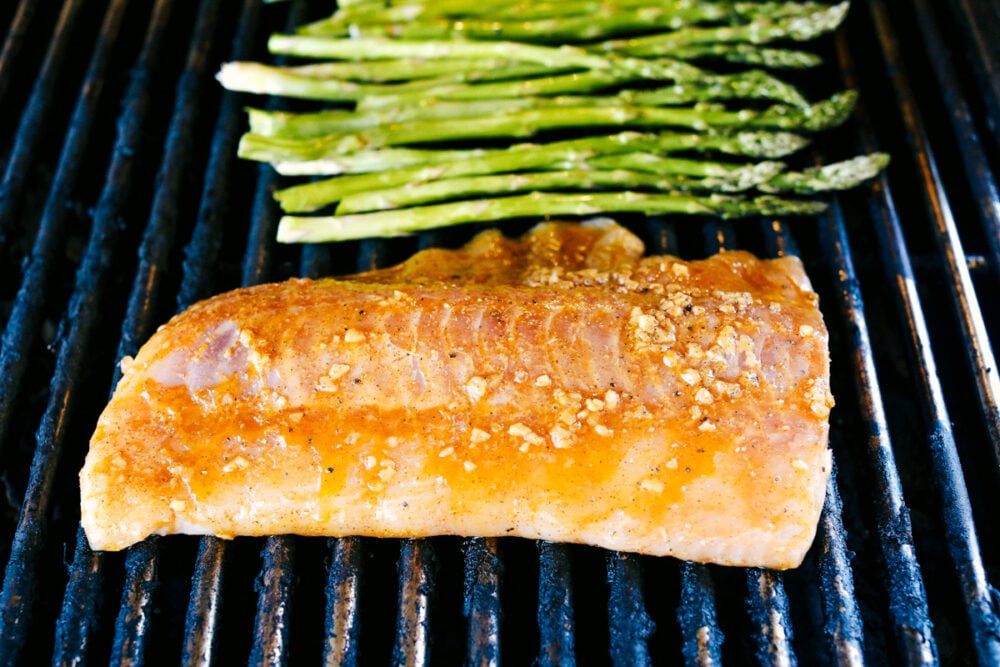 This Grilled Cajun Garlic Butter Cod is the only recipe you will need this summer! The cod is tender and juicy and the flavor is spicy and buttery, it's insanely delicious! Cod and Asparagus on the grill cooking.