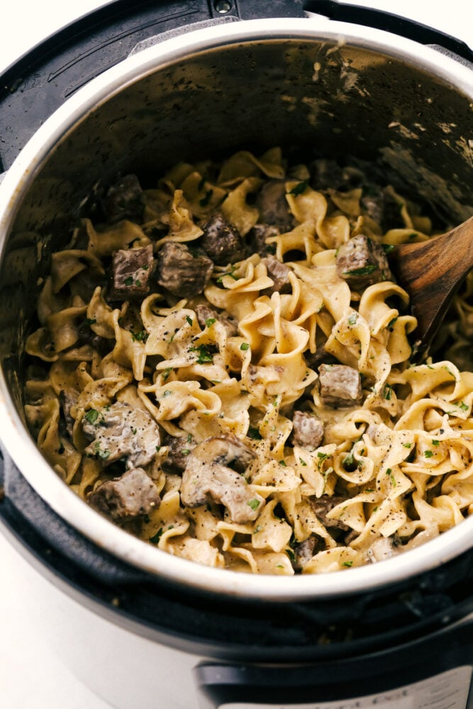 Instant Pot Beef Stroganoff creates the most tender, full flavored stroganoff I've ever had! Made hands off in the instant pot, this creamy dish is going to be your favorite way to cook it! Instant Pot Stroganoff being stirred with a wooden spoon.