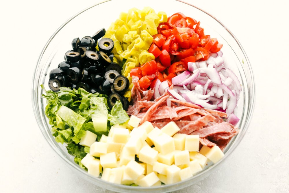 Italian Chopped Salad is stuffed with flavor and texture that is highly satisfying. Full of classic Italian flavors, this salad is going to be a huge hit at your next gathering! Ingredients for Italian chopped salad in a clear bowl, ready to be mixed.