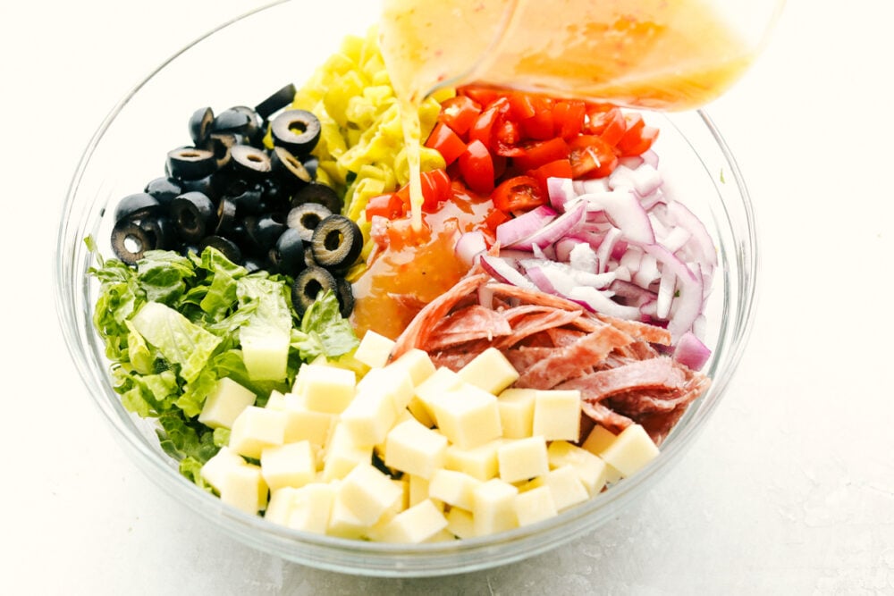 Italian Chopped Salad is stuffed with flavor and texture that is highly satisfying. Full of classic Italian flavors, this salad is going to be a huge hit at your next gathering! Pouring the dressing over the salad ingredients.