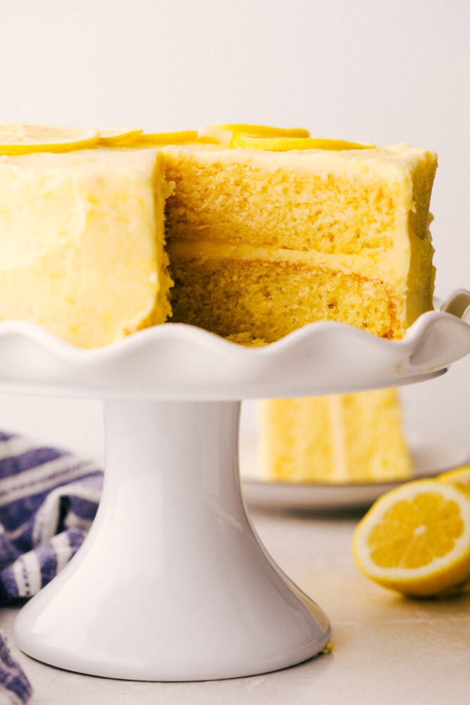 Lemon Cake is everything you want in a sweet, yet zingy cake! Tender moist layers of refreshing lemon cake are smothered with a tart but sweet frosting. Lemon Layered Cake on a pedestal cake platter.