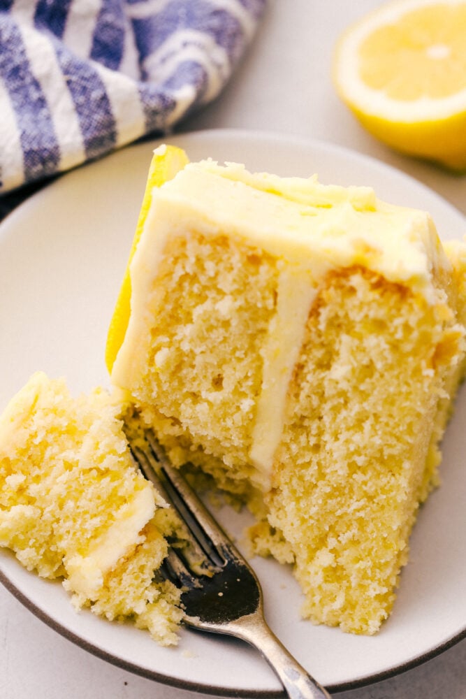 Lemon Cake is everything you want in a sweet, yet zingy cake! Tender moist layers of refreshing lemon cake are smothered with a tart but sweet frosting. Using a fork to take a bite of the cake with lemon frosting.