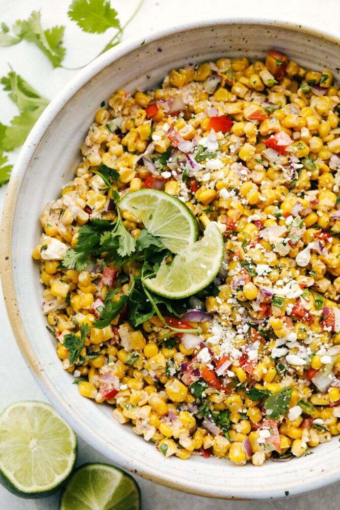 This Amazing Mexican Corn Salad is hands down an all time summer favorite. Full of fresh, bright, zingy and spicy flavors, it has something for everyone! Mexican Corn Salad garnished with limes and cilantro.