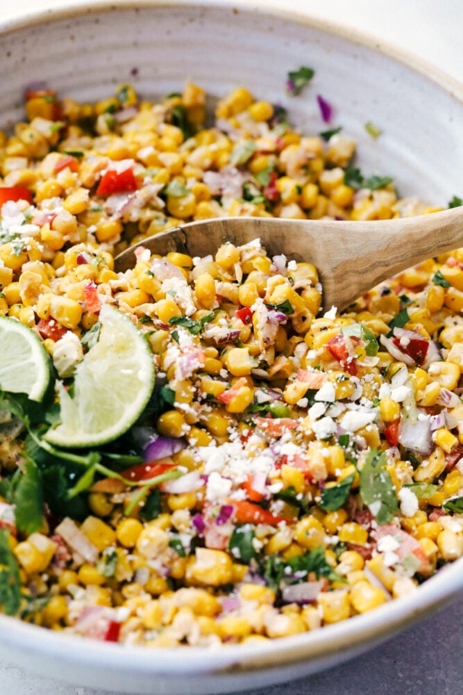 This Amazing Mexican Corn Salad is hands down an all time summer favorite. Full of fresh, bright, zingy and spicy flavors, it has something for everyone! Stirring the salad together and serving it on a wooden spoon.