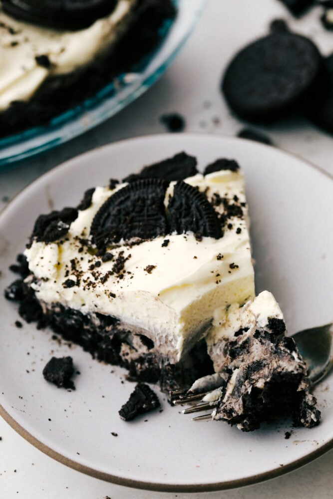 This No-Bake Oreo Pie is going to steal the show! It's so quick and easy you might find yourself making it everyday! A slice of oreo pie on a plate, garnished with oreos.