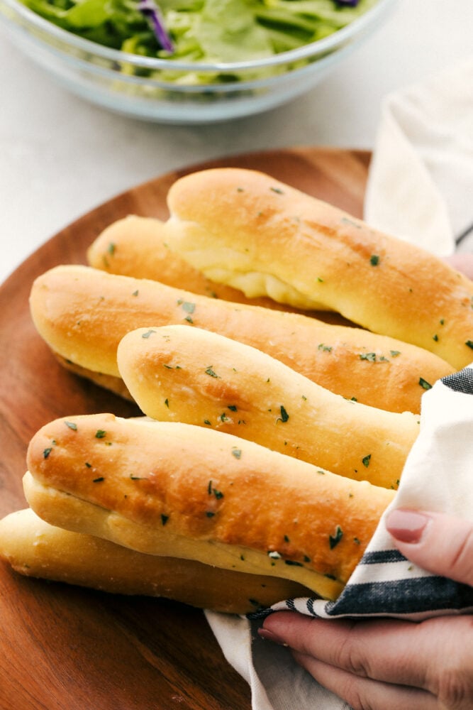 These copycat Olive Garden Breadsticks are insanely delicious! Fresh, buttery, and garlicky you can still have unlimited breadsticks, only these taste better! Placing breadsticks on a board wrapped in a towel and ready to eat.