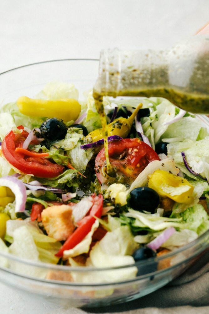Olive Garden Salad Dressing is one of the best things at the restaurant, and now you can make it at home! Instead of having to go to the restaurant, you can have this tasty dressing anytime you crave it in the comfort of your own home! Pouring the olive garden salad dressing over a salad.