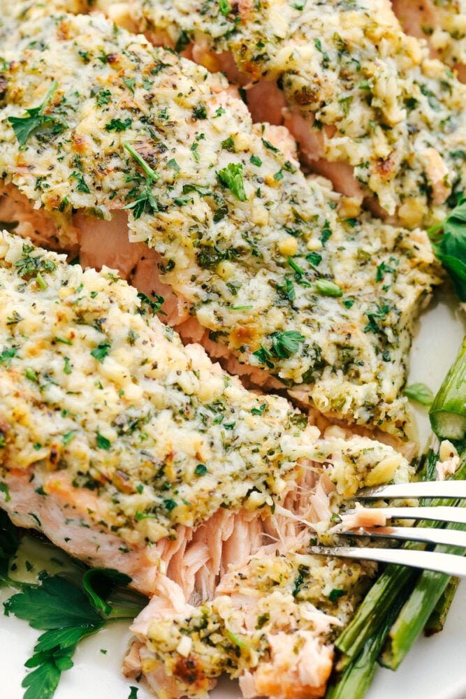 Salmon that is baked in foil and brushed in a Parmesan Garlic Herb Marinade. It seals in the amazing flavor and cooks the salmon to tender and flaky perfection! Using a fork to flake off a bite of salmon crusted with parmesan and garlic.