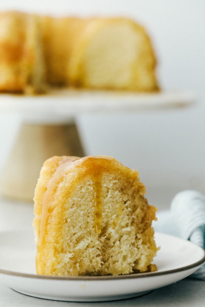 Rum Cake is a rich dense cake that is overflowing with butter rum flavor that is insanely delicious. This cake is moist and the rum syrup adds a layer of decadence that is next level amazing! Rum cake slice on plate with rum sauce on top.