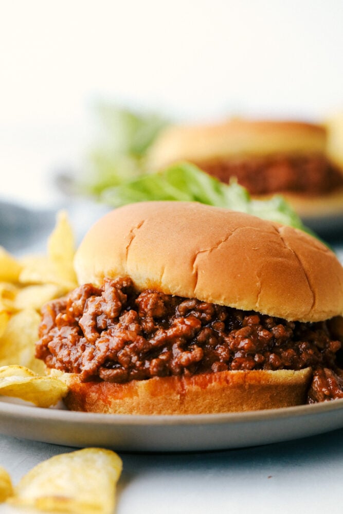 Delicious Sloppy Joes are messy, saucy and the perfect family dinner. A timeless classic, these are bound to be the best you have ever had! A sloppy joe on a plate with potato chips.