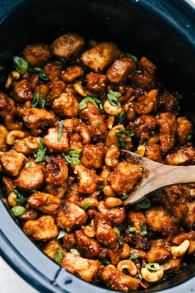 This amazing slow cooker cashew chicken is way better than takeout! The chicken is breaded to perfection, the sauce is full of flavor and the cashews hidden throughout are the best part! Stirring the cashew chicken in the slow cooker.