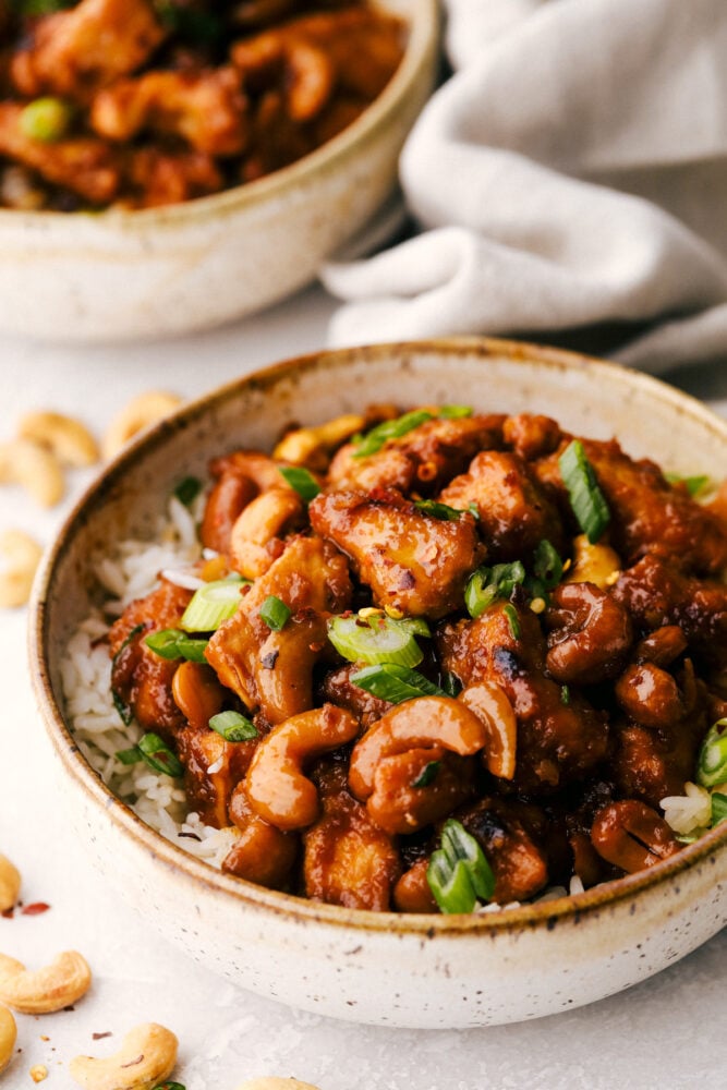 This amazing slow cooker cashew chicken is way better than takeout! The chicken is breaded to perfection, the sauce is full of flavor and the cashews hidden throughout are the best part! A bowl of cashew chicken on top of a bed of rice.