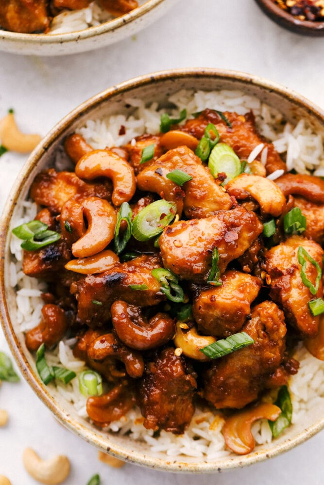 This amazing slow cooker cashew chicken is way better than takeout! The chicken is breaded to perfection, the sauce is full of flavor and the cashews hidden throughout are the best part! Sitting on a bed of rice, slow cooker cashew chicken in a bowl.