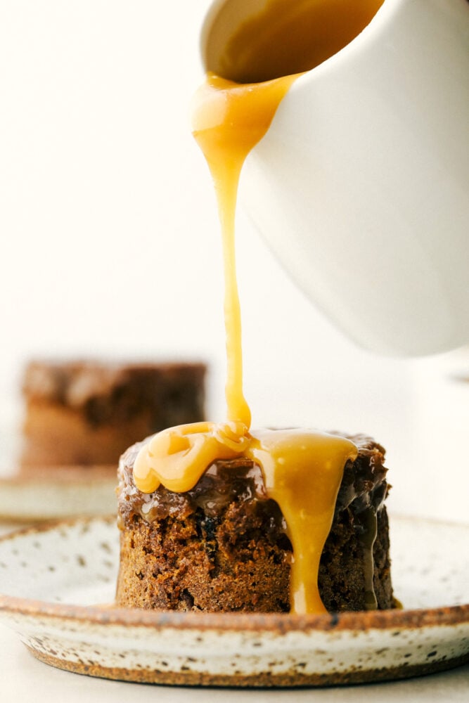 Sticky Toffee Pudding is an English dessert that you are going to absolutely love! This moist sponge cake contains finely chopped dates, a rich toffee sauce, and served with vanilla ice cream. Pouring toffee sauce over the sticky pudding.