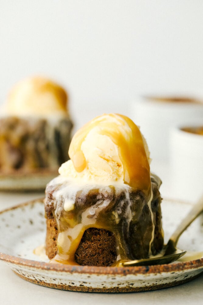 Sticky Toffee Pudding is an English dessert that you are going to absolutely love! This moist sponge cake contains finely chopped dates, a rich toffee sauce, and served with vanilla ice cream. A plate with sticky toffee pudding and a scoop of vanilla ice cream.
