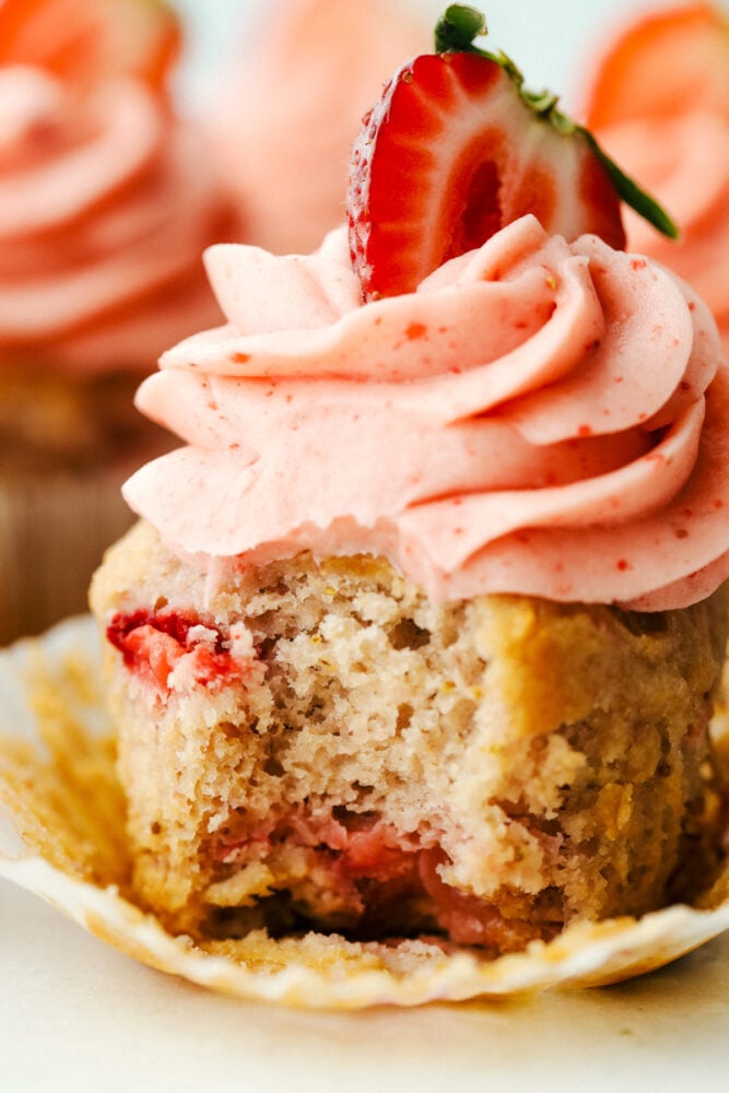 Strawberry Cupcakes are made with fresh and freeze-dried strawberries to create an incredible burst of flavor. Pretty and pink, these cupcakes are sure to be the perfect treat. A bite from a cupcake.