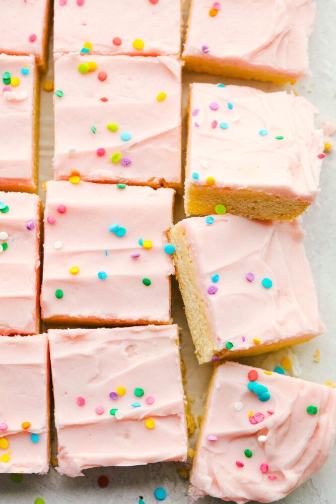 These sugar cookie bars are soft and sweet with a smooth layer of icing that is sprinkled on top. Perfect for your next party! Sugar cookie bars cut into squares.