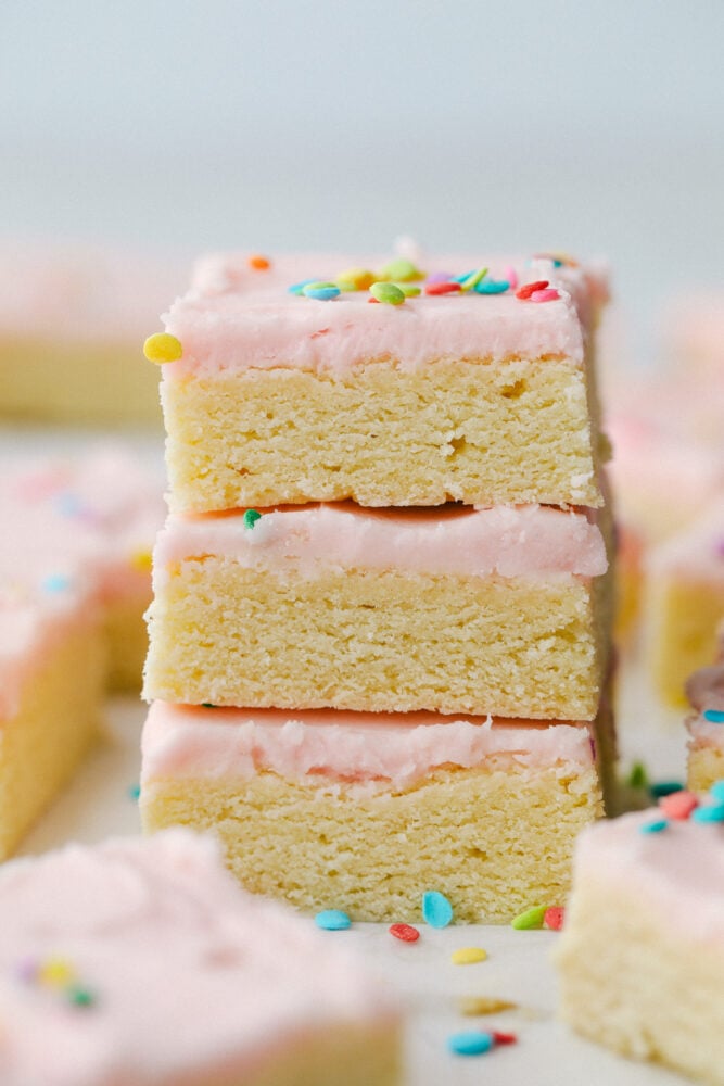 These sugar cookie bars are soft and sweet with a smooth layer of icing that is sprinkled on top. Perfect for your next party! Three sugar cookie bars stacked on top of each other.