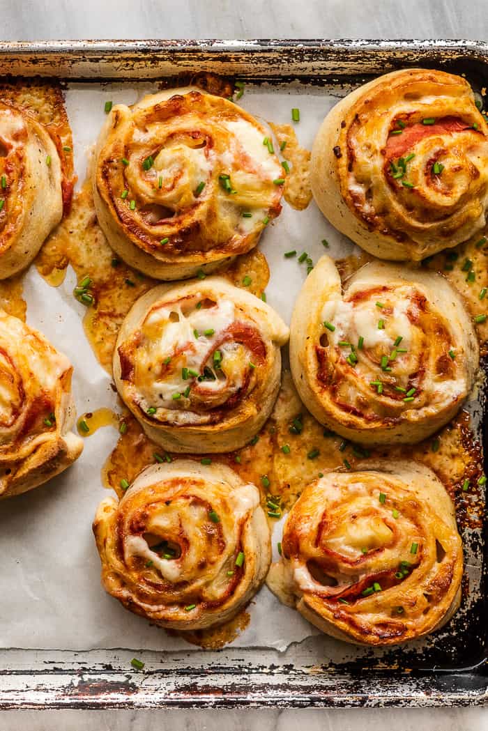 Pizza pinwheels are a super easy, family-friendly lunch or dinner. They're made with soft pizza dough and your favorite toppings rolled up then sliced into rounds. Once they're baked, they become cheesy and delicious bites that your whole family will love. Ham and pineapple pizza pinwheels on a baking sheet.