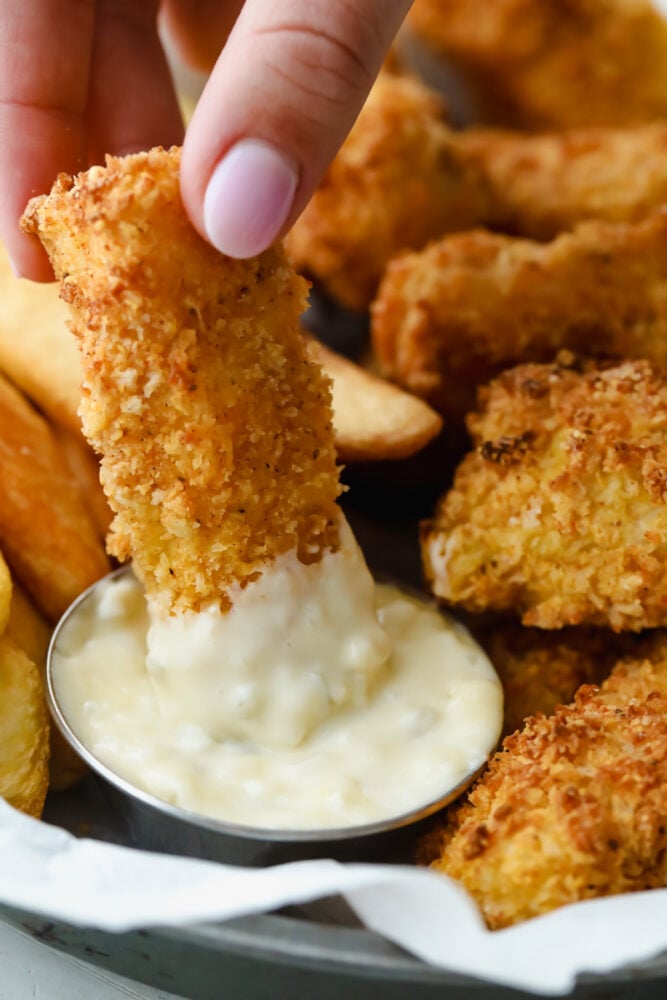 These air fryer fish sticks are going to rock your family's world. Never again will you make fish sticks from a box, these are insanely delicious! Dipping a homemade fish stick in tartar sauce.