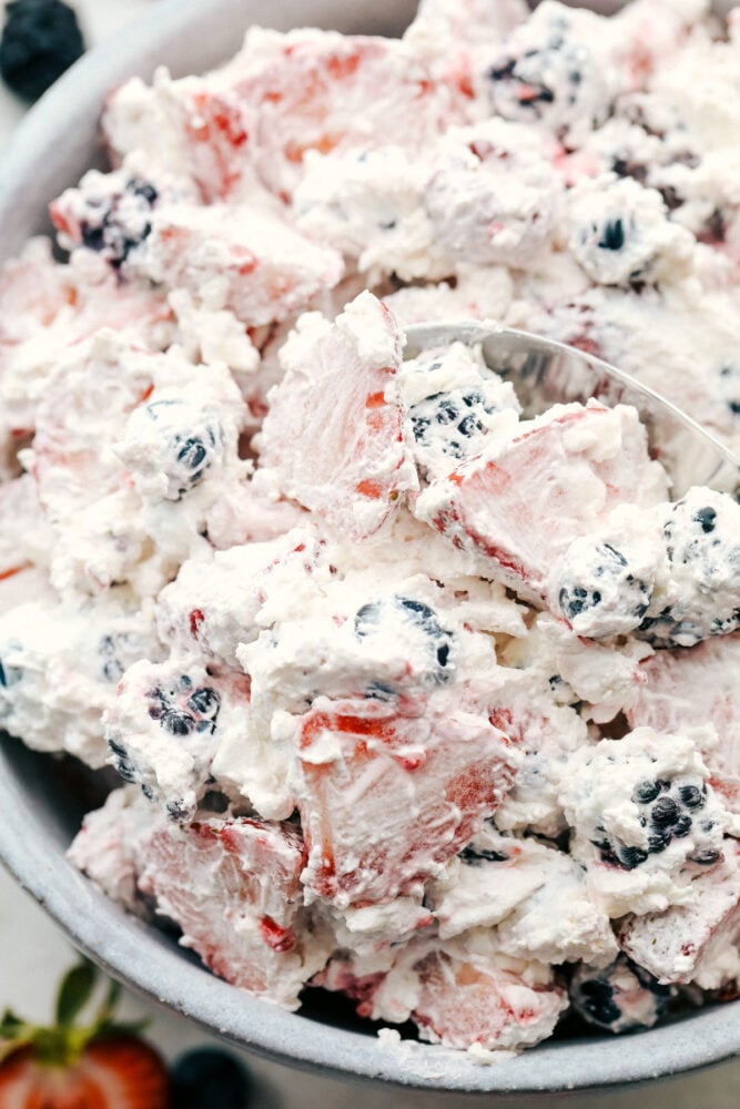 Berryย Cheesecake Salad has only the freshest berries combined with a creamy cheesecake fluff. ย This is so amazingย and will be the hit of any gathering! Scooping the berry cheesecake with a spoon.