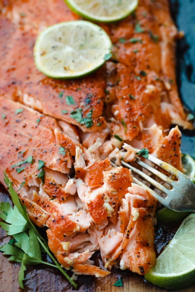 Smoky, woodsy flavors meet summery honey and lime in this melt-in-your-mouth salmon recipe! You are not going to be able to get enough of this irresistible Cedar Plank Honey Lime Salmon! Salmon being cut with a fork.