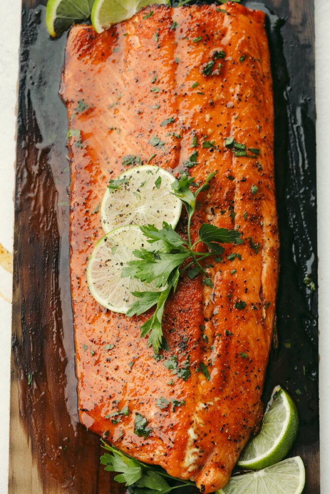 Smoky, woodsy flavors meet summery honey and lime in this melt-in-your-mouth salmon recipe! You are not going to be able to get enough of this irresistible Cedar Plank Honey Lime Salmon! Grilled salmon on cedar plank with garnish.