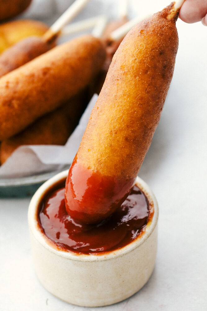 Homemade corn dogs are crispy golden on the outside and perfectly cooked on the inside. These are super easy to make at home and the whole family is going to love how they taste! Dunking a corndog in ketchup.