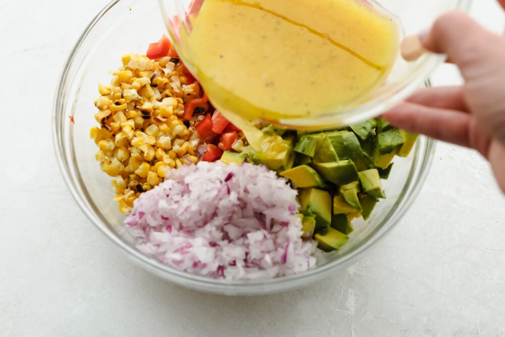 Don't let the name fool you, this Summer Corn Salad definitely can (and should be!) enjoyed all year round! It's a fresh corn salad made with onion, bell pepper, avocado, and.....corn! Fresh or frozen corn will work Pouring the dressing over the salad.