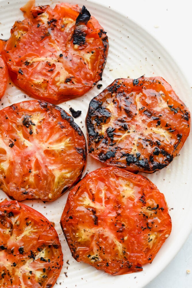 Super easy and super delicious, you are going to love these juicy Grilled Tomatoes! Each slice is cooked to perfection and bursting with luscious, savory flavors in every bite. Grilled tomatoes on plate