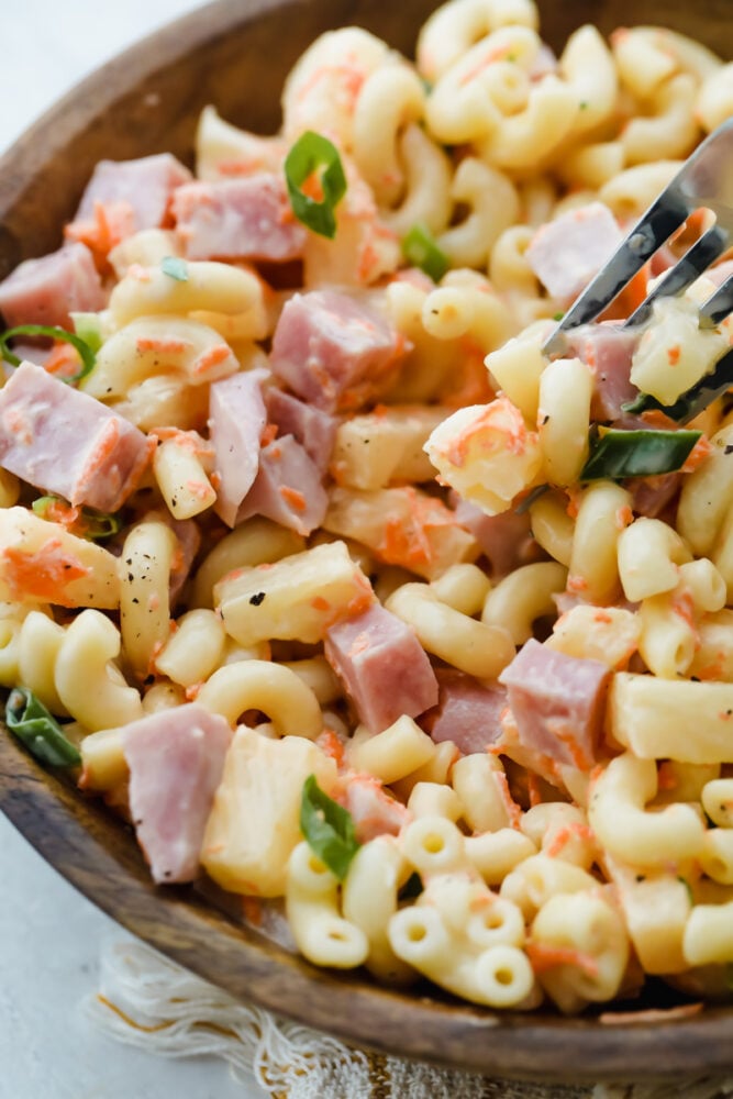 Hawaiian Macaroni Salad is the perfect side dish! It is a delicious macaroni pasta salad with ham, pineapple, shredded carrots, and green onions, and a tangy dressing. Scooping a bite of the macaroni salad with a fork.