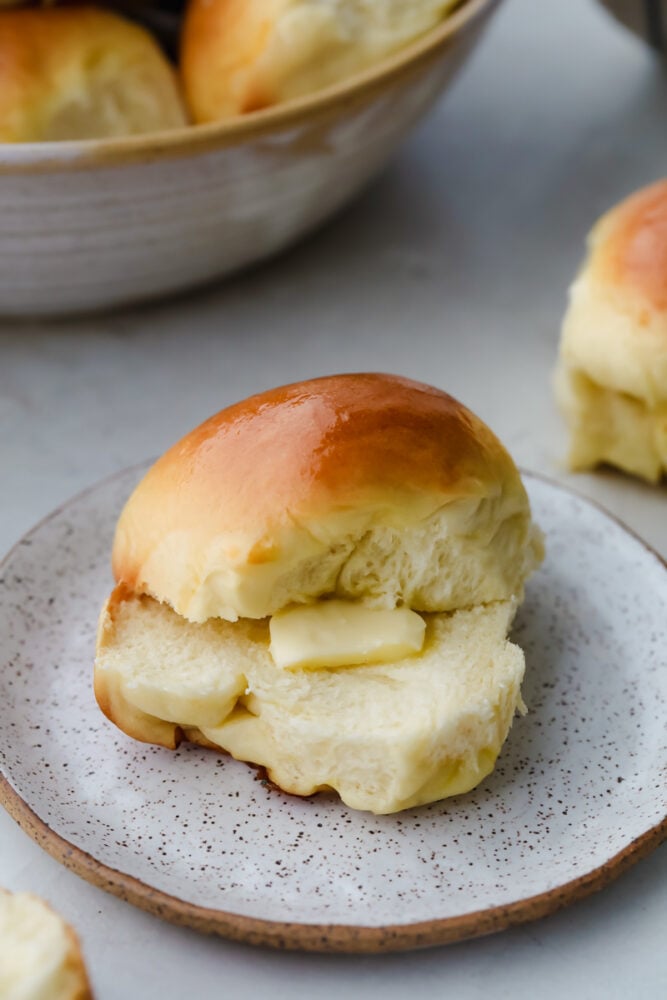 Moist, fluffy Hawaiian Sweet Rolls are a staple you will want to use for all your weekday meals. Whether you use them for sliders, sides, or just eat them as-is like me, they will be gone in no time with how sweet and buttery-soft they are! Hawaiian Roll cut in half with dollop of butter.