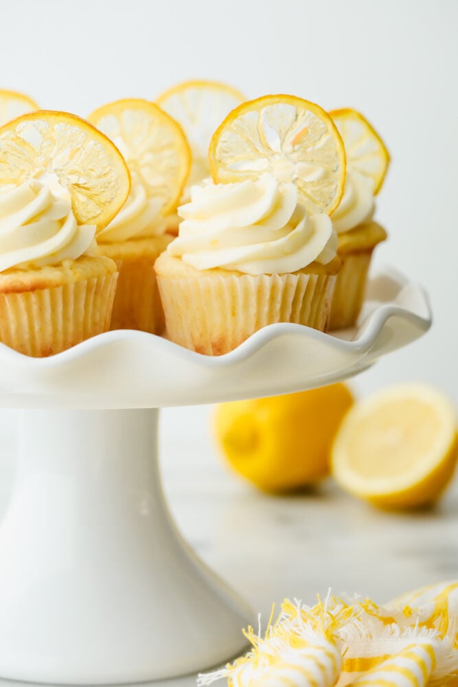 The AMAZING sweet and zesty flavors of these Lemon Cupcakes will have you hooked! Fresh lemon adds a pinch of summer to a classic, decadent treat. Lemon cupcakes with garnish on a serving platter.