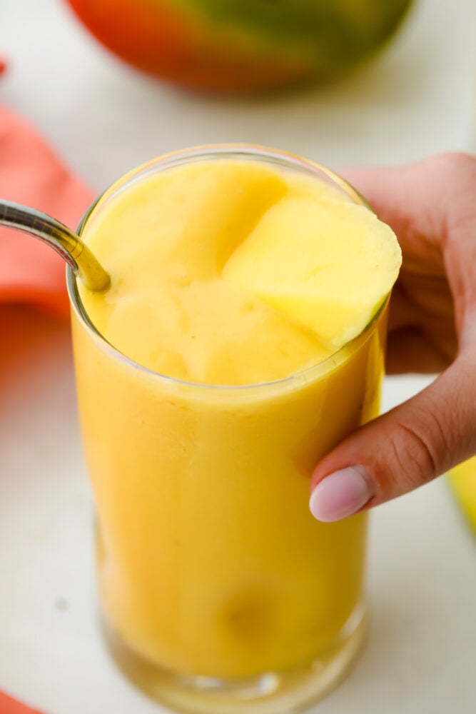 Mango Smoothie is a cool refreshing summertime treat you are going to love! Sweetened with banana and honey, this is summer in a glass Picking up the glass of mango smoothie getting ready to drink.