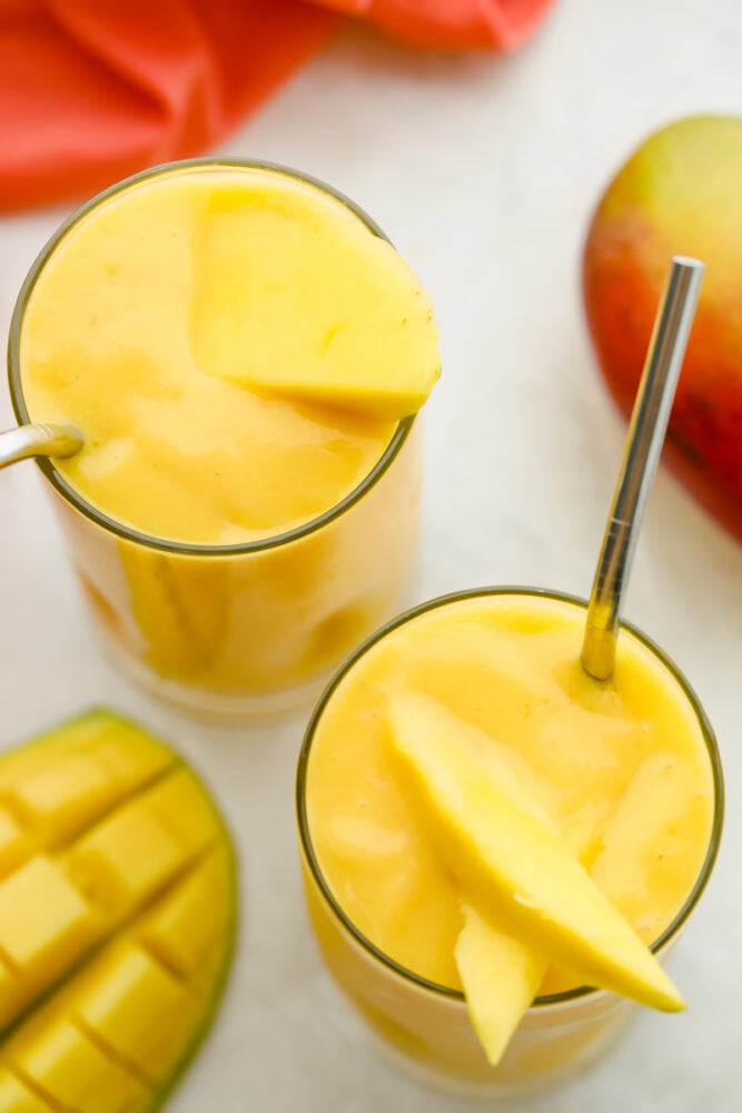 Mango Smoothie is a cool refreshing summertime treat you are going to love! Sweetened with banana and honey, this is summer in a glass Top of view of a thick creamy smoothie garnished with fresh mango.