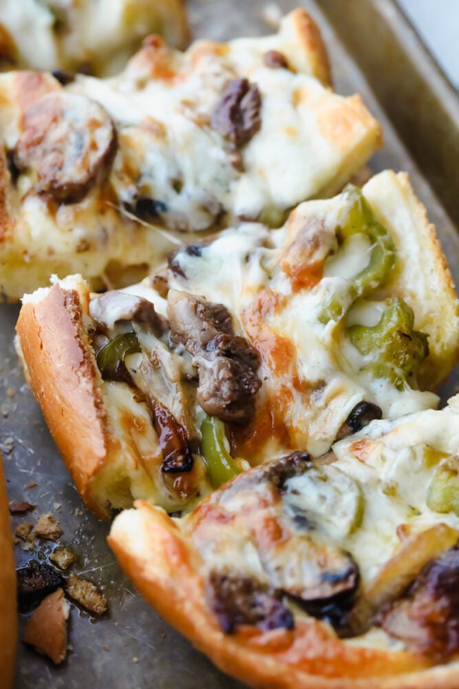Philly Cheese Steak Cheesy Bread with just a few simple ingredients is the taste of Philly for a crowd! It comes together in just minutes with major flavor in each bite! Philly Cheesesteak Cheesy Bread cut into pieces