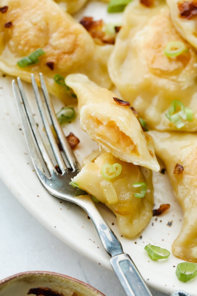 Pierogi are delightful dumplings stuffed with potatoes and cheese. These are traditional Polish dumpling that puts a whole new meaning to comfort food! Cutting into a pierogi with a fork showing the potato and cheese filling.