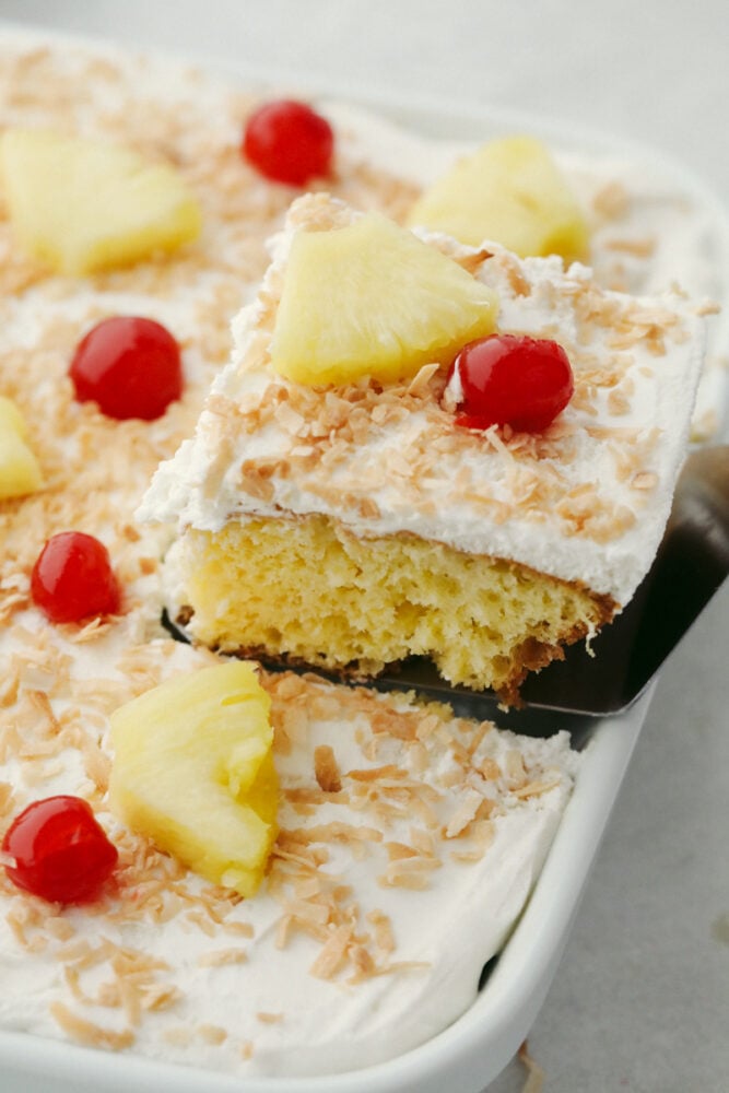 Pina Colada Poke Cake is a little slice of tropical paradise on a plate! Rich in flavor this is a light fluffy cake everyone is going to love! Removing a slice of cake from the pan to serve.