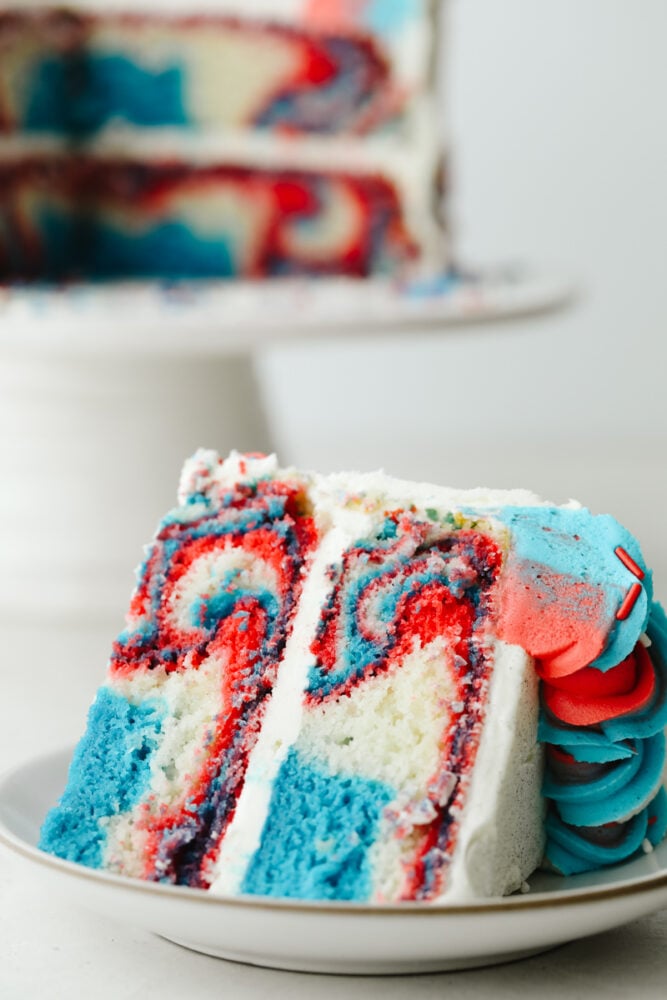 This Red, White and Blue Cake is going to steal the show for your 4th of July celebrations! Tender moist cake is swirled in the sweetest tie-dye pattern! A slice of the red white and blue cake showing the swirls.