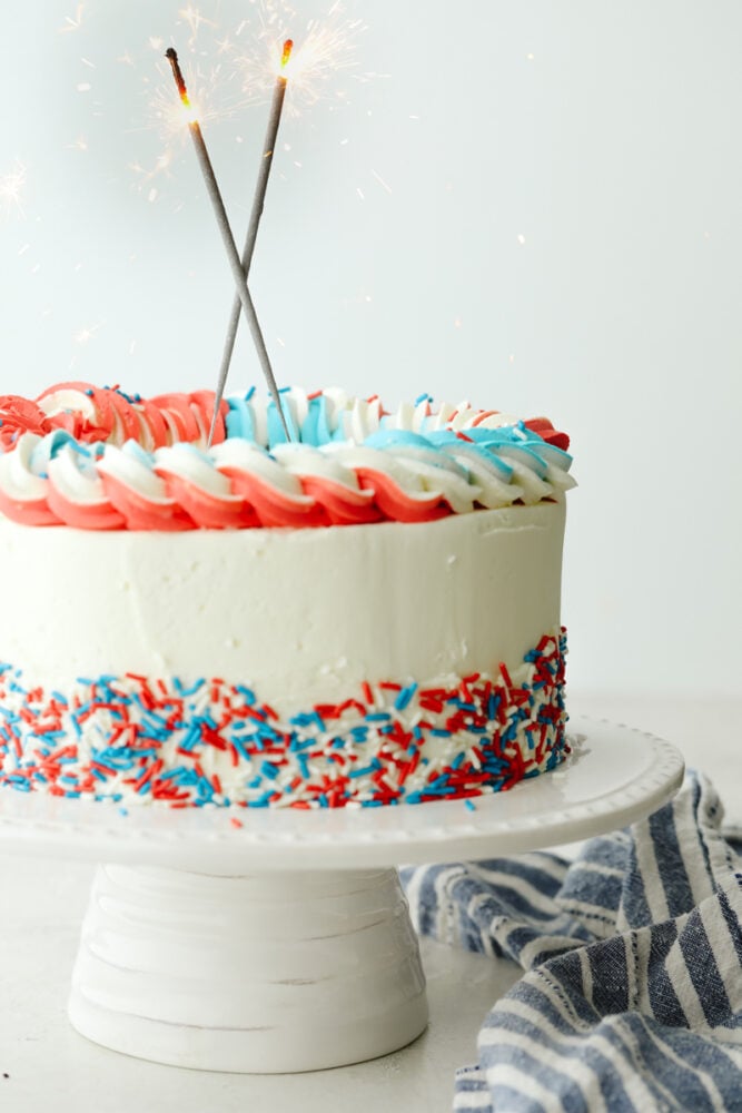 This Red, White and Blue Cake is going to steal the show for your 4th of July celebrations! Tender moist cake is swirled in the sweetest tie-dye pattern! Decorated cake with sparklers on top.