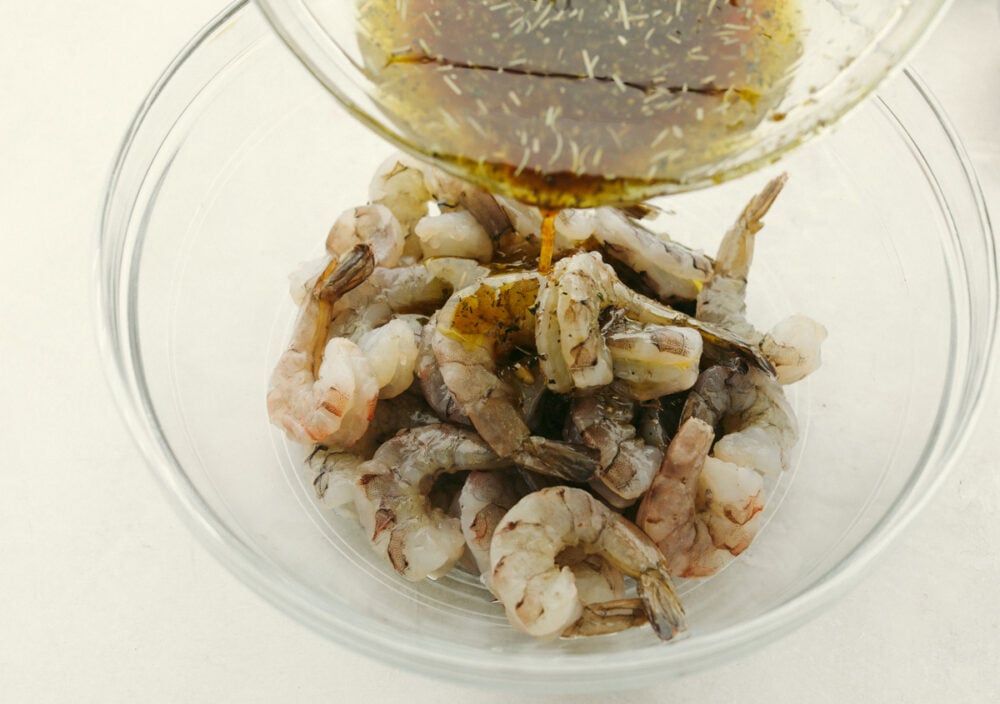 Layer this amazing marinade onto your shrimp for a perfectly rich, savory flavor with a pop of lemon your taste buds will LOVE! The drool-worthy flavor combinations and ease of preparation make this Shrimp Marinade a recipe to come back to over and over again. Pouring marinade over raw shrimp.