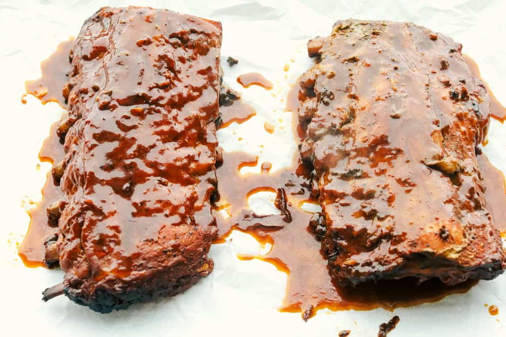 Myย Slow Cooker Ribsย are hands-down one of my favorite recipes on the site! They fall off the bone, are coated in sticky-sweet sauce, and are unbelievably easy to make. Cooked ribs on a baking sheet with sauce from crockpot poured over the top.