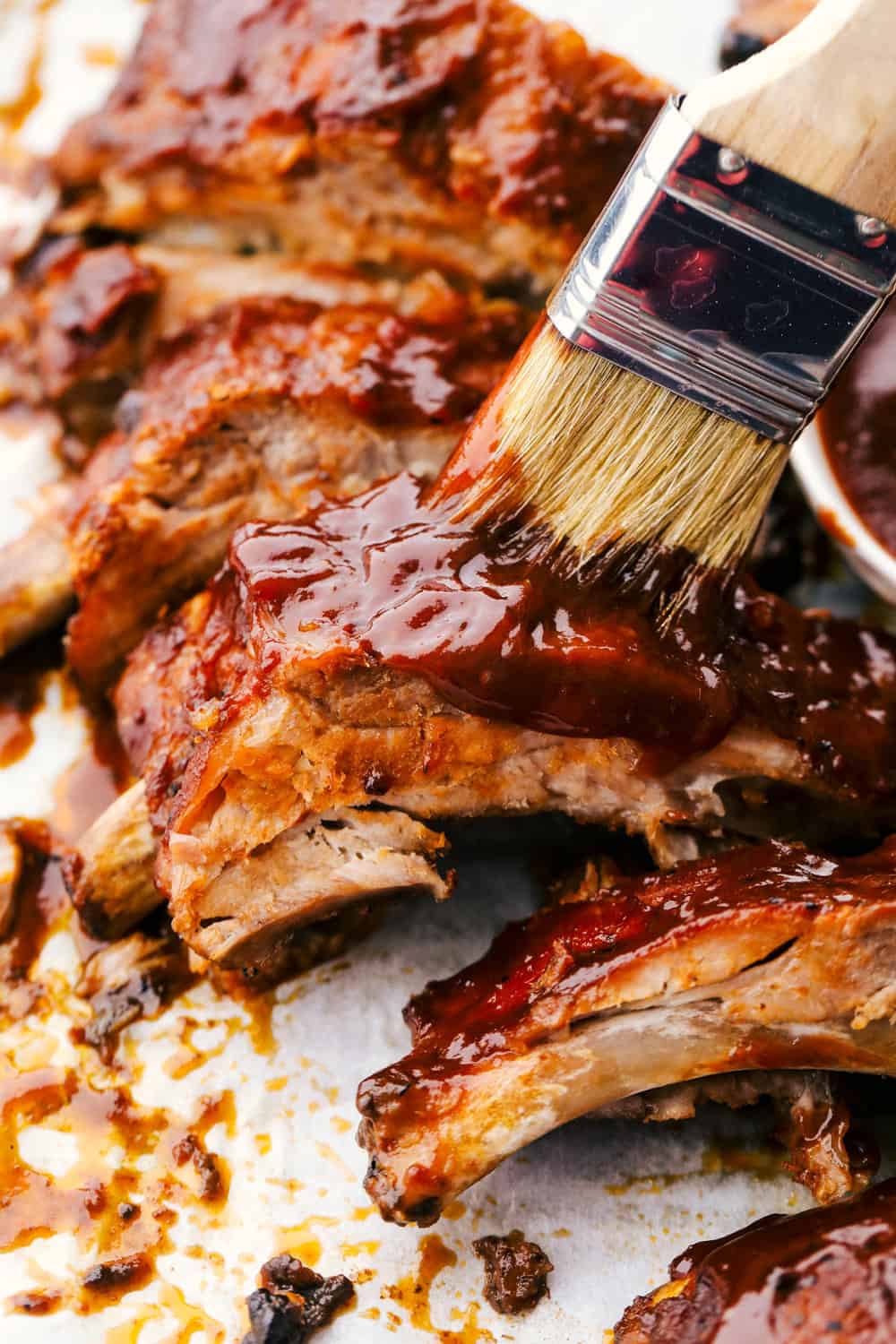 Myย Slow Cooker Ribsย are hands-down one of my favorite recipes on the site! They fall off the bone, are coated in sticky-sweet sauce, and are unbelievably easy to make. Someone spreading extra BBQ sauce on the cooked ribs.