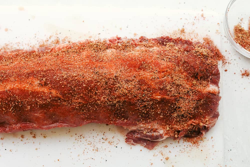 Myย Slow Cooker Ribsย are hands-down one of my favorite recipes on the site! They fall off the bone, are coated in sticky-sweet sauce, and are unbelievably easy to make. Rib rack with seasoning rubbed all over.