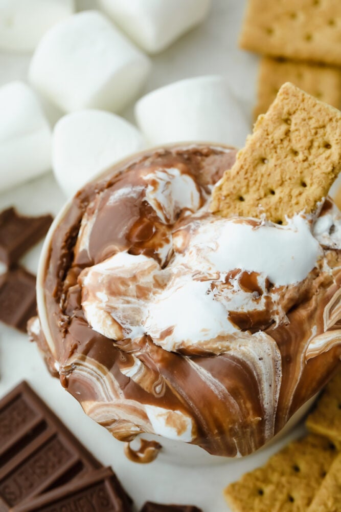 S'mores Dip is an easy way to get all the ooey gooey goodness from a s'more without the roasting! This is such a fun sweet treat that everyone can enjoy without building a hot fire A graham cracker sittin g a pot of s'more dip.