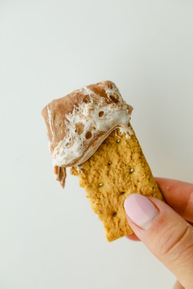 S'mores Dip is an easy way to get all the ooey gooey goodness from a s'more without the roasting! This is such a fun sweet treat that everyone can enjoy without building a hot fire A bit of graham cracker with the s'more dip on it.
