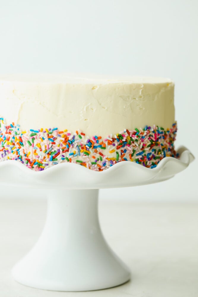The Absolute Best White Cake is a recipe you will come back to time and time again for a delicious and beautiful result. Fluffy, moist, and soft, this really is a cake to impress! Frosted white cake with sprinkles added.
