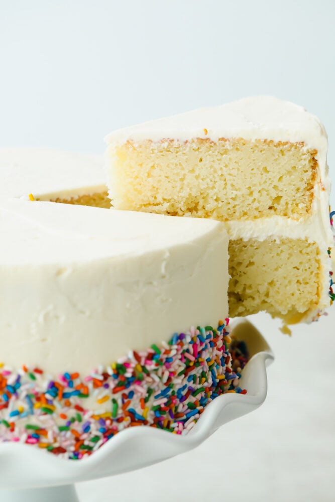 This white cake is a recipe you will come back to time and time again for a delicious and beautiful result. Fluffy, moist, and soft, this really is a cake to impress! A slice of white cake cut and taken out of the cake.